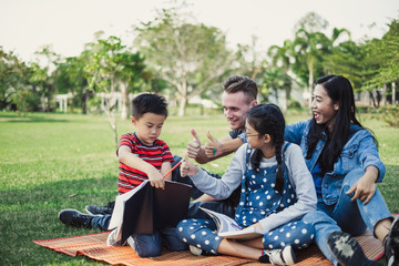 Happy family of asian and caucasian laying on garden green park outdoor for playing and replaxing on holiday