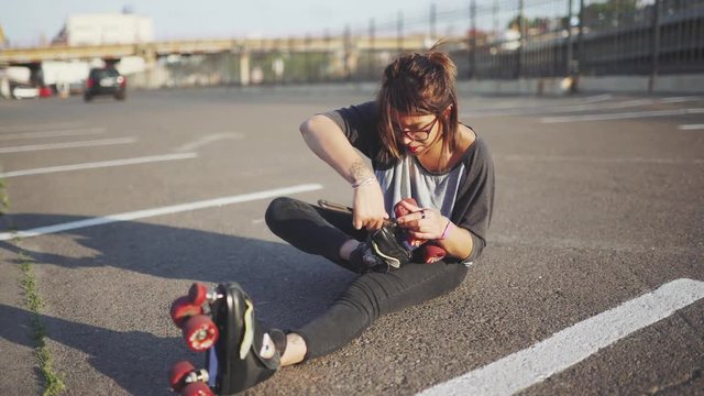 attractive hipster female  fix roller skates on the street at sunset