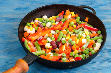Frying pan with frozen vegetables on blue background