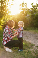 Fototapeta premium Mother and son in plaid shirts. Woman buttoning shirt boy. Family time together.