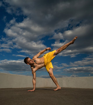 Tricking on street. Martial arts. Man kick with hand support barefoot. Shooted from bottom foreshortening against sky.