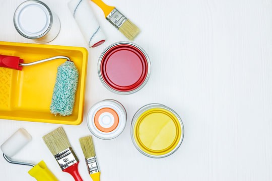 painting tools on white wooden background. paintbrushes, rollers, tray, cans with red, yellow, orange paint. flat view