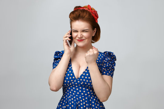 Celebration, success and victory. Joyful successful pin up girl in elegant retro outfit having phone converation in studio using mobile, making winning gesture with clenched fist, exclaiming Yes