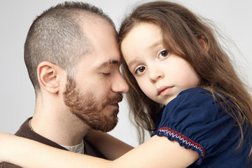 Love, family bonding and affection concept. Close up shot of attractive young Caucasian guy with stylish beard hugging his sad beautiful baby girl, closing eyes, expressing care and tenderness
