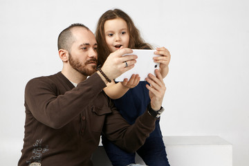 People, electronics, gadgets and connection concept. Emotional female child opening mouth widely, amazed with new digital tablet, using it with her fashionable modern young father with stubble