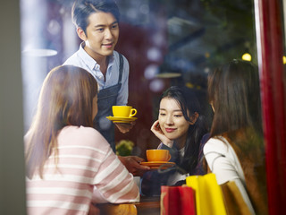 young asian waiter serving coffee to customers