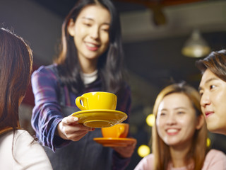 young smiling asian waitress serving coffee to customers