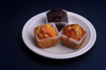 Multiple types of delicious muffin on top of a ceramic plate with dark background.