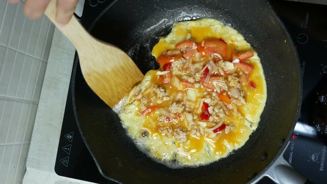 flip over cooking omelet,  chicken egg with mince pork , red onion, tomato in  the black teflon induction pan. Top view. fried with wooden turner. Air bubble in pan. 