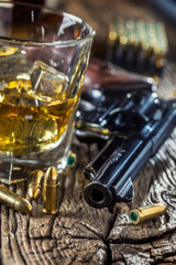 Glass of whiskey cognac or bourbon with revolver and bullets on wooden table