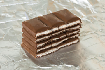 Stack of milk chocolate bar slices on silver foil background.