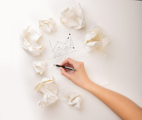 Female hand next to a few crumpled paper balls drawing a progress chart