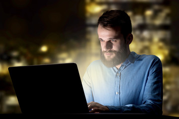 Young handsome businessman working late at night in the office with city lights in the background