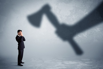 Businessman afraid of a huge shadow hand holding an axe concept on background