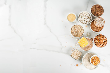 Selection various types cereal grains groats  in different bowl on white marble background, above copy space