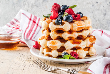 Belgian waffles with raspberries, blueberries and syrup, homemade healthy breakfast, light concrete background copy space