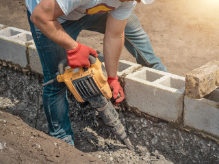 Worker with a jackhammer, foundation, building blocks.
