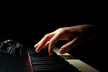 Hand playing a piano keyboard with black background