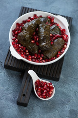 White plate with dolmades or dolma and pomegranate seeds on a black wooden serving board, blue stone background, studio shot