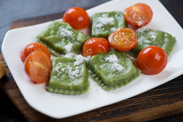 Close-up of spinach ravioli with cherry tomatoes and grated parmesan served on a white plate, studio shot