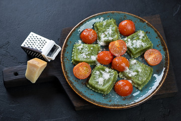 Turquoise plate with italian spinach ravioli on a black wooden serving board, horizontal shot over black stone background