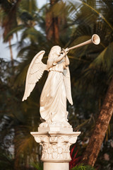 The angel in white with big wings blows the trumpet in dawn beams - a sculpture near Catholic...