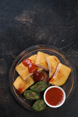 Sliced chicken cordon bleu with vegetable nuggets and sauce, flat-lay over dark brown stone background, vertical shot with space