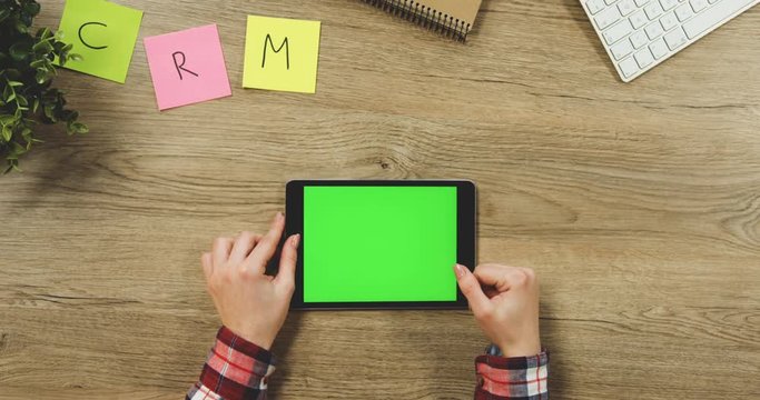 Close up on the woman's hands taping on the black horizontal tablet device with a green screen on the wooden table. SRM. Chroma key.