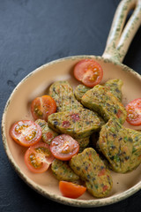 Close-up of fried vegetable nuggets with cherry tomatoes in a serving pan, vertical shot