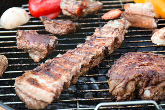 Appetizing juicy spare ribs and vegetables on barbecue grill, close up