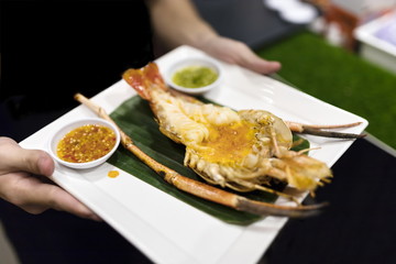 The waiter served a plate of grilled  prawn on the banana leaf and Thai spicy sauce. Selective focus.
