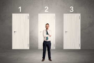 Fototapeta premium Businessman in grey room with three numbered white door behind his back 
