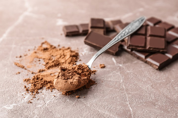 Spoon with cocoa powder and tasty chocolate on table
