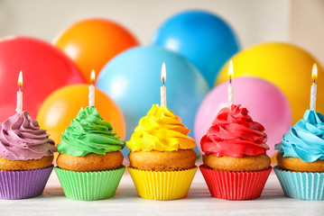Delicious birthday cupcakes with candles and blurred balloons on background