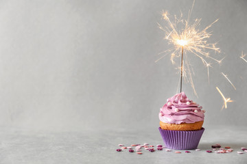 Delicious birthday cupcake with sparkler on grey background