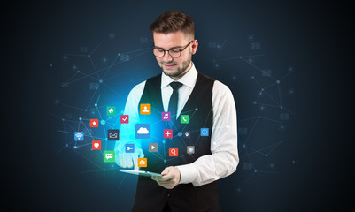 Handsome businessman in suit with tablet on his hand and application icons above
