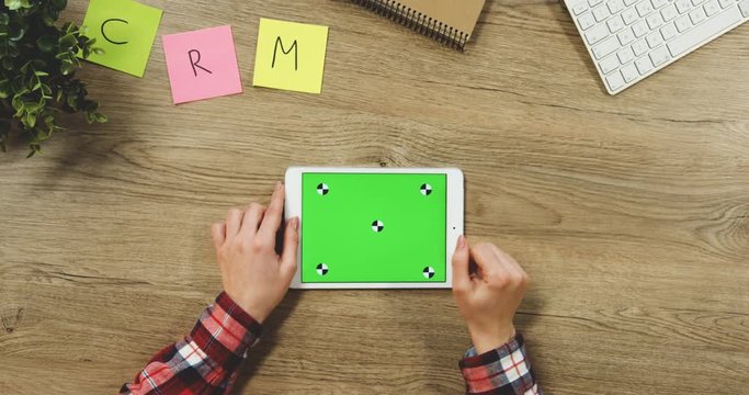 Close up on the woman's hands taping on the white horizontal tablet device with a green screen on the wooden table. SRM. Chroma key. Tracking motion