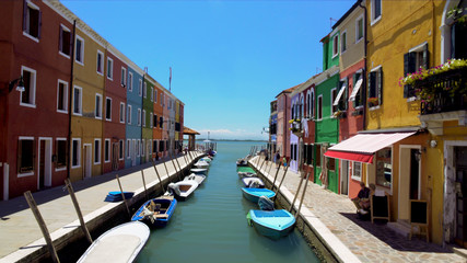 Fototapeta na wymiar Colorful houses and boats moored along canal on Burano island, locals in street