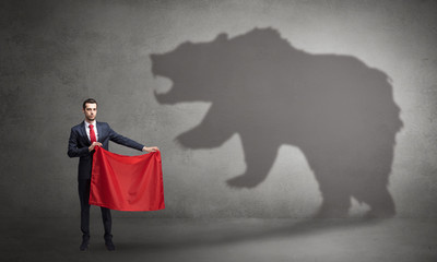 Businessman standing with red cloth in his hand and big bear shadow on his background
