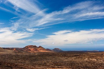 Fototapeta na wymiar Volcanic crater in the Timanfaya National Park under a blue sky with clouds. Lanzarote, Canary Islands, Spain.