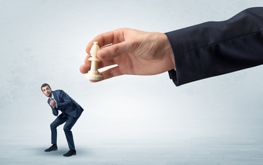 Big hand holding chessman and down little afraid businessman concept in a light space
