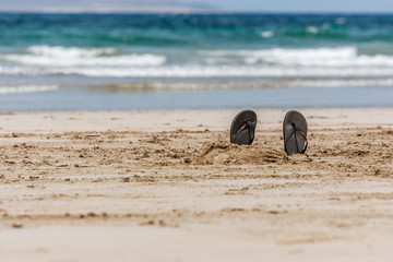 Flip-Flops in the sand with blue sea and waves on the background. La Graciosa, Lanzarote, Canary Islands, Spain.