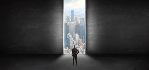 Businessman standing in a dark room and looking outside to a cityscape view
