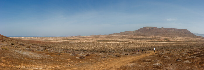 Panoramic view of tourists on mountain bikes under a volcanic crater. La Graciosa, Lanzarote, Canary Islands, Spain.