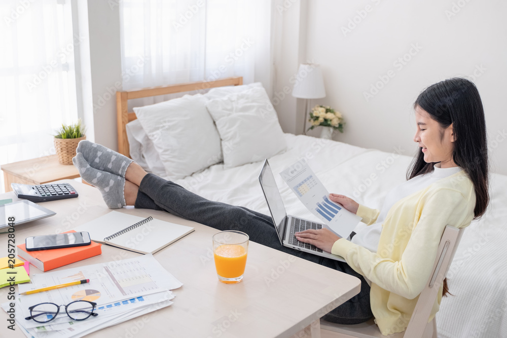 Poster asian female freelancer reading report paper and working with laptop lay on knee with rest leg on ta