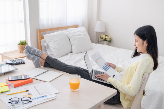Asian female freelancer reading report paper and working with laptop lay on knee with rest leg on table in bedroom at home.Work at home concept.work from home.relax lifestyle.