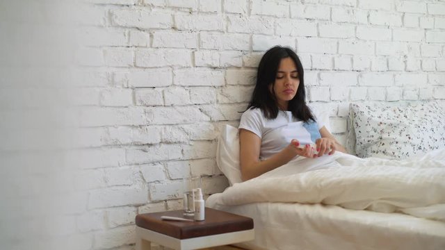 Young woman taking pills lying on the bed. Accept tablets. Disease.
