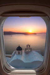 Fototapeta premium Amazing sunset at Panagia Theoskepasti, on the Skaros rock at Imerovigli, Santorini, Greece through a frame of plane window.