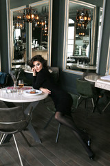 woman with dark curly hair in elegant dress sitting in elegant restaurant