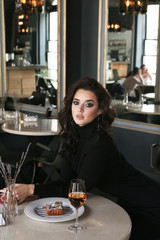 woman with dark curly hair in elegant dress sitting in elegant restaurant